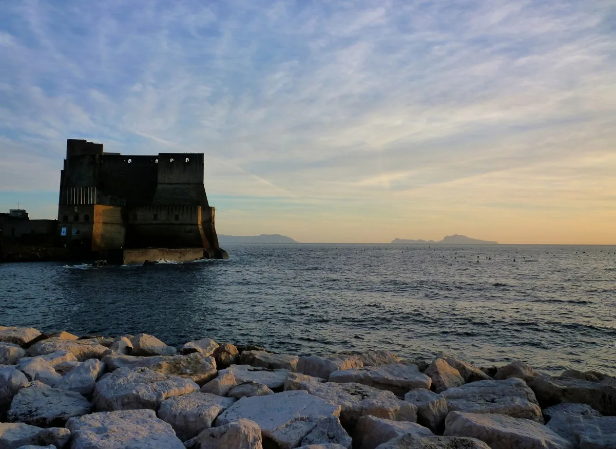 Castel dell'Ovo silhouetted at sunset, with Capri faint on the horizon