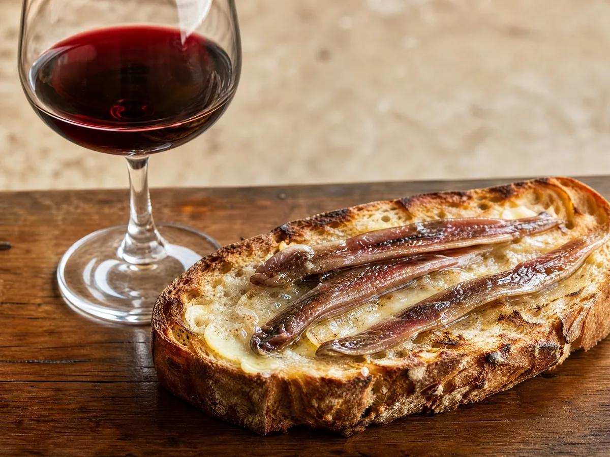 A glass of red wine with toast, butter and salted anchovies