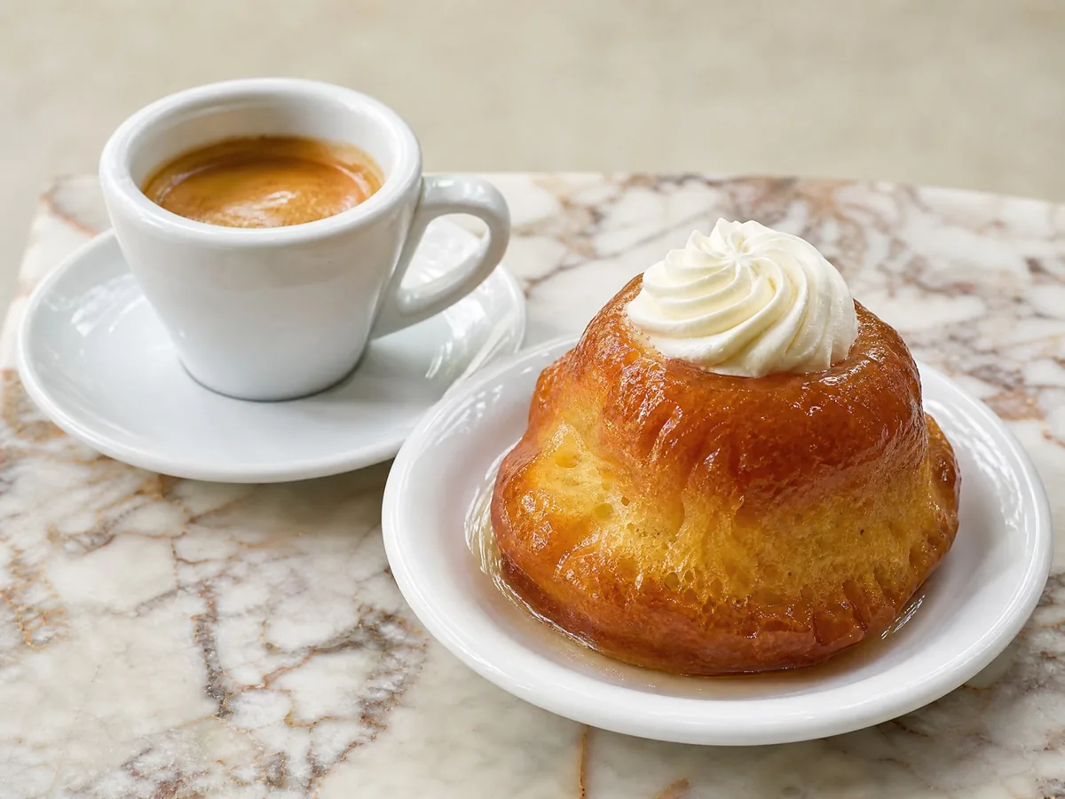 An espresso beside a rum baba on a marble café table