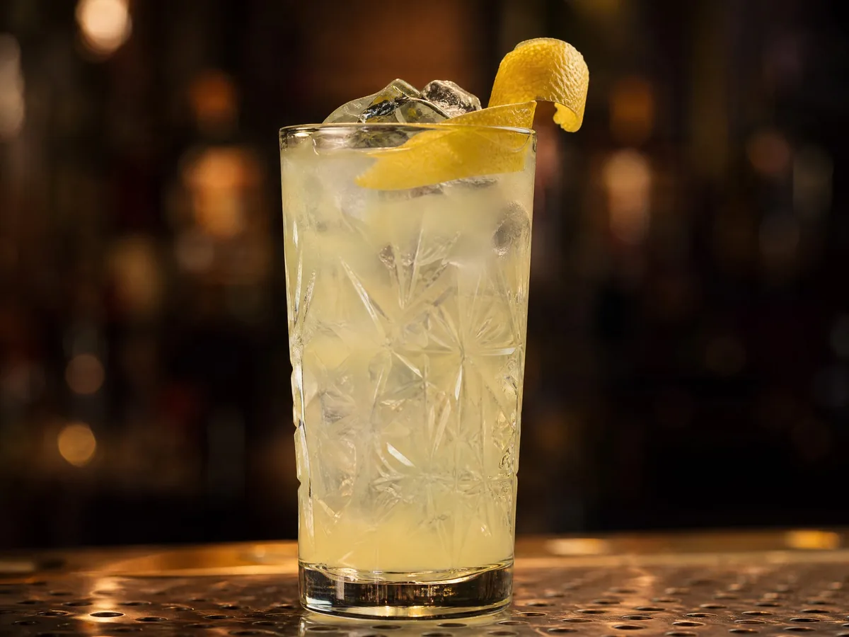 A pale citrus gin cocktail over ice with a curl of lemon peel