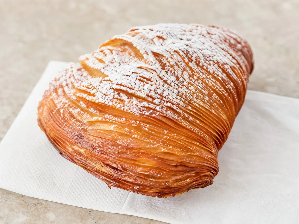 A warm sfogliatella riccia dusted with icing sugar on a napkin