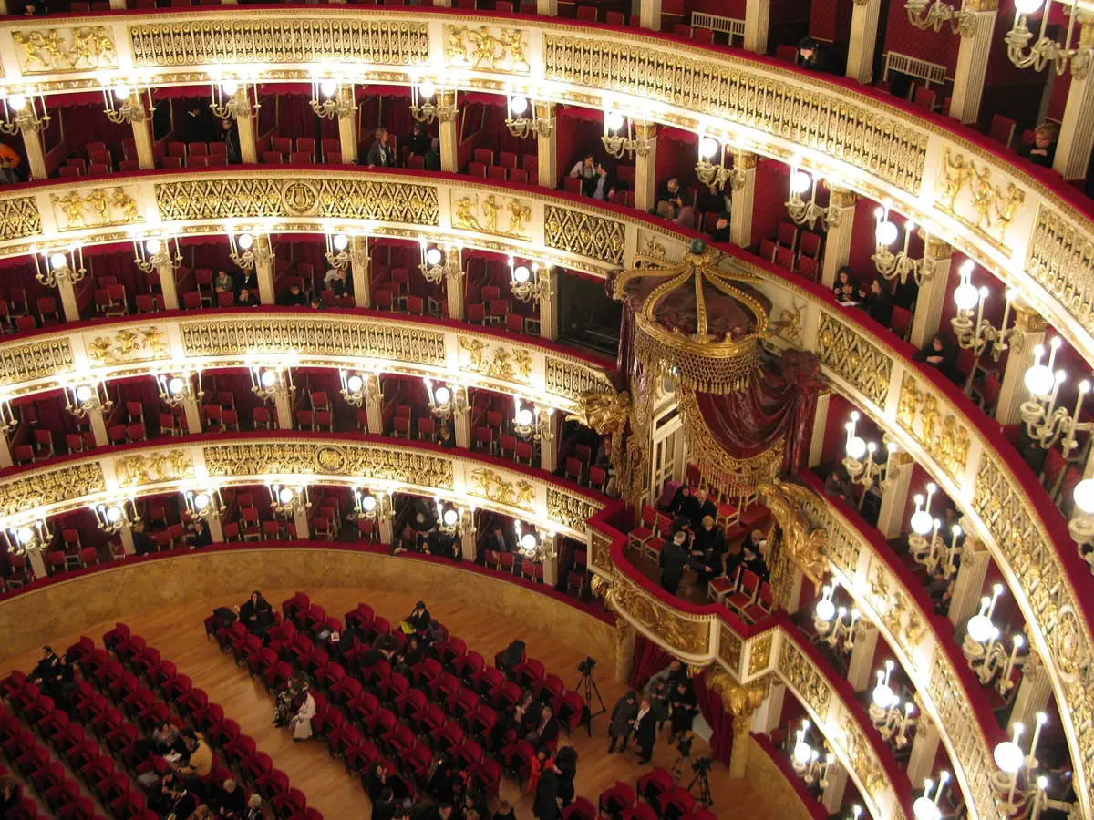 Red and gold tiers of boxes inside the Teatro di San Carlo filling with an audience
