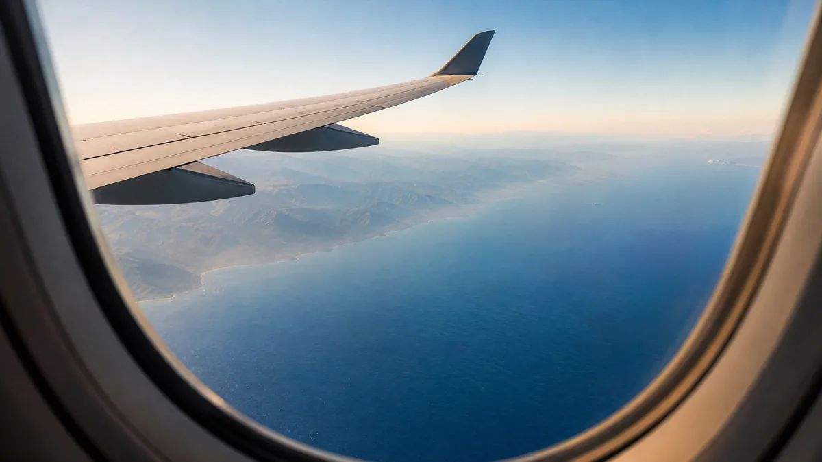 The wing of a plane over a blue sea and a hazy mountain coast