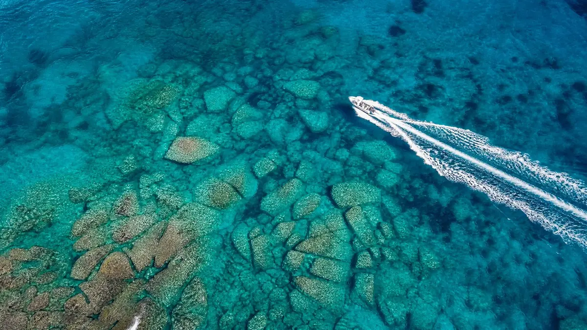 A small motorboat cutting a white wake across turquoise sea, seen from above