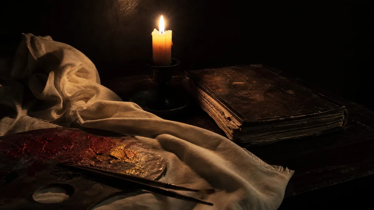 Une nature morte à la bougie avec un tissu, un livre et une palette de peintre dans l'ombre
