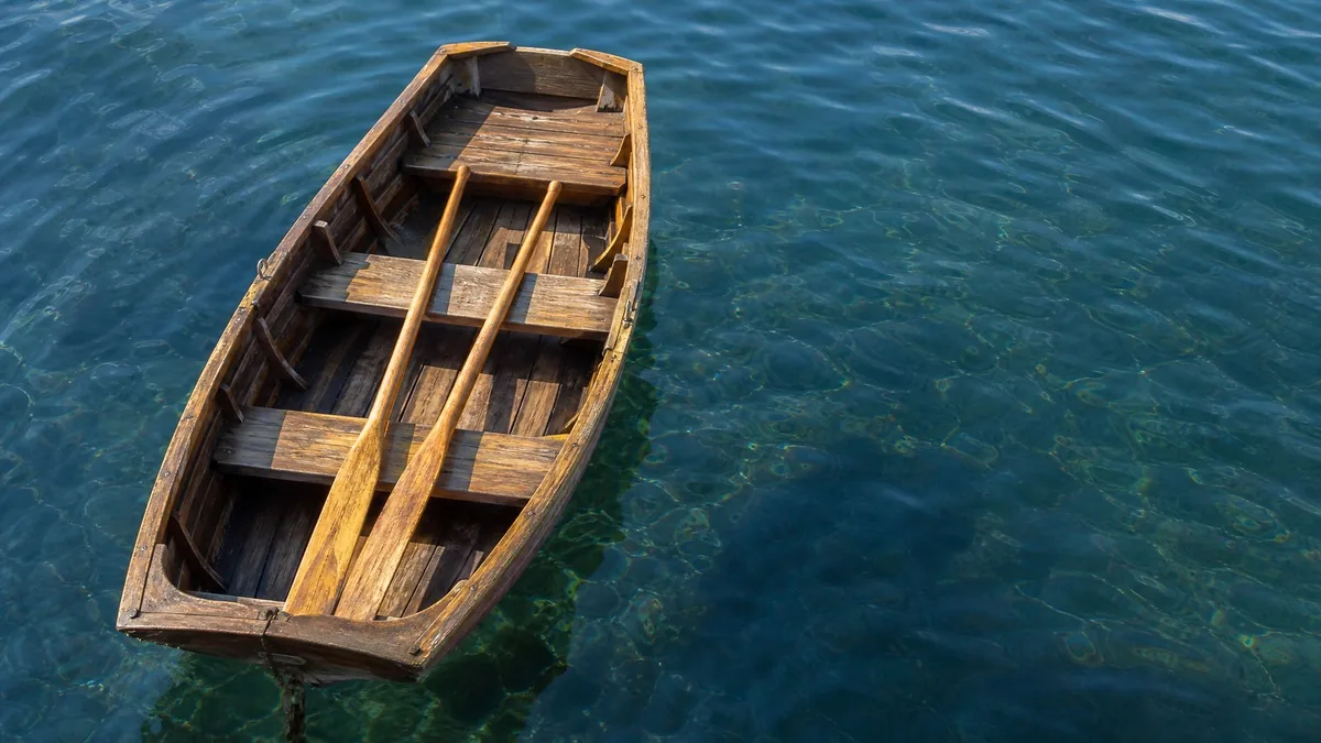 Ein kleines Holz-Ruderboot mit Rudern auf tiefblauem, ruhigem Wasser