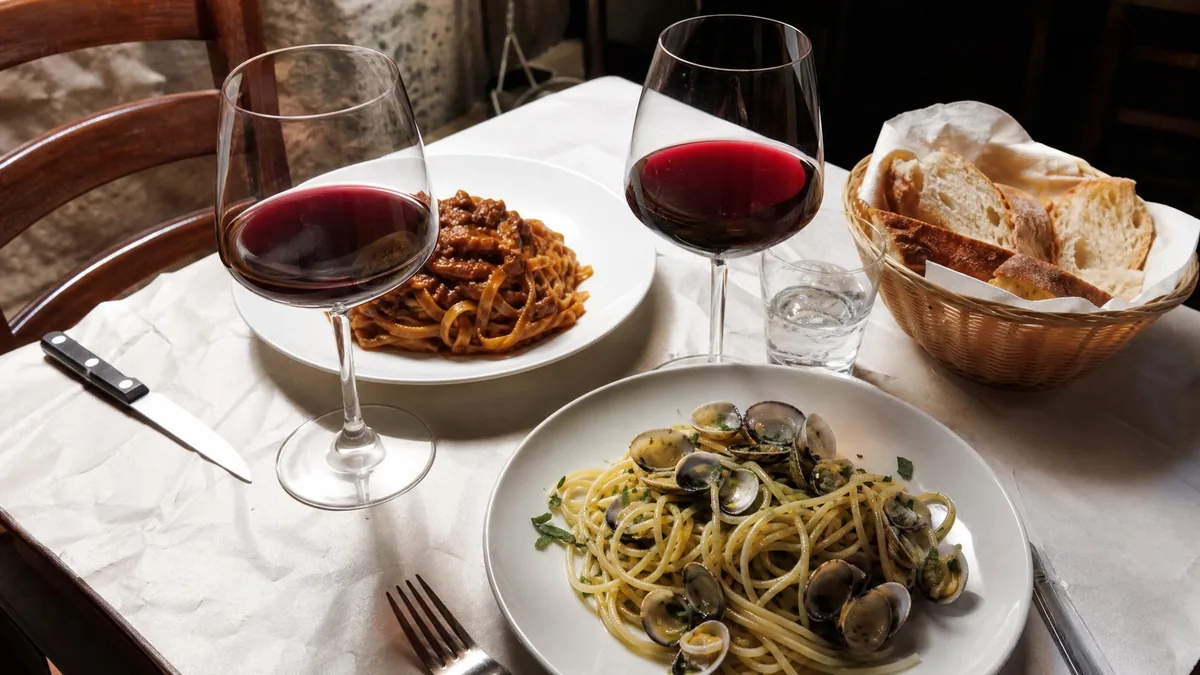 Une table de trattoria avec des pâtes au ragù, des spaghetti aux palourdes, du pain et du vin rouge