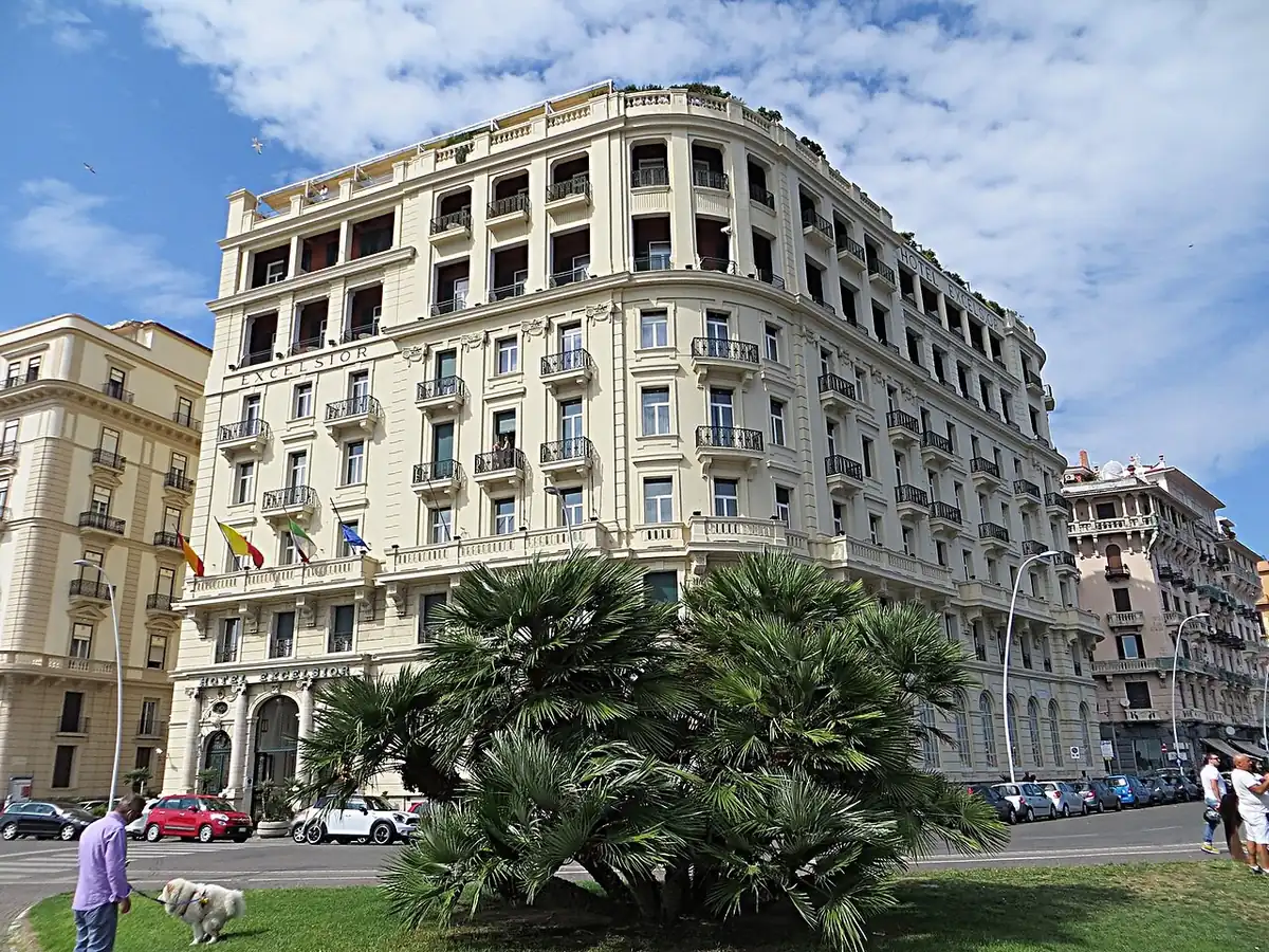 Das weiße Belle-Epoque-Gebäude des Hotel Excelsior an der neapolitanischen Uferpromenade, hinter Palmen