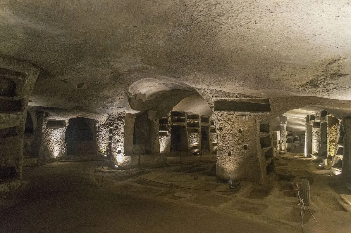 Salle souterraine éclairée des Catacombes de San Gennaro avec des niches funéraires creusées dans le tuf