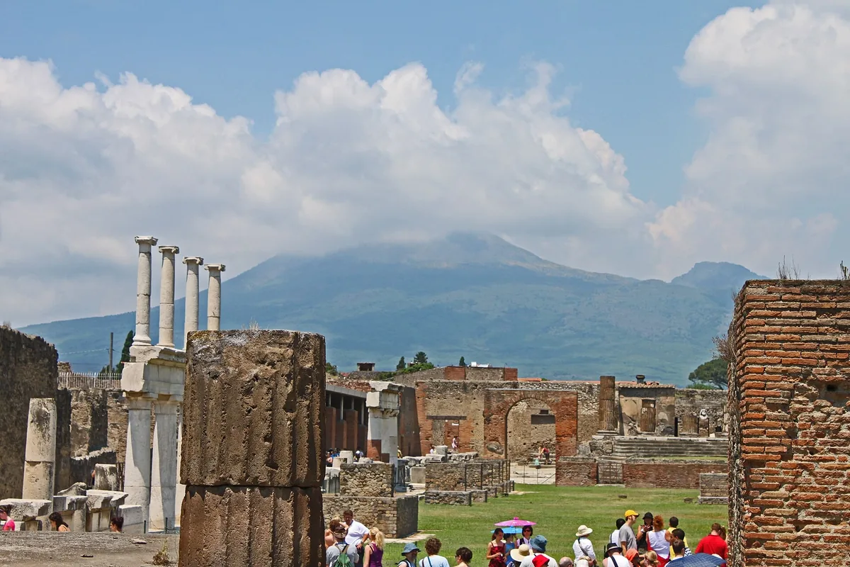 Columns in the Forum of Pompeii with Vesuvius behind and tourists among the ruins